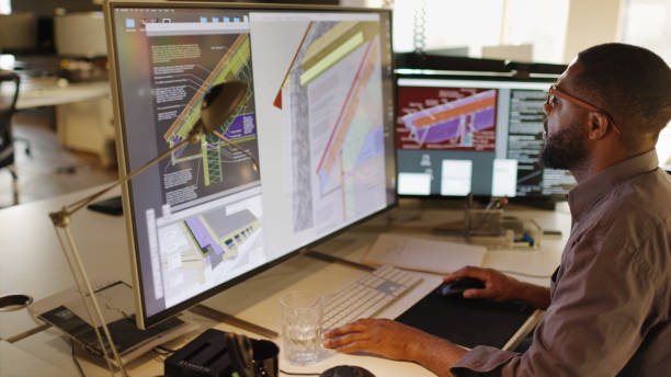 Stock Photograph of an African American / Afro-Caribbean male working with large computer screens & compute Aided design. He’s designing built in insulation structures in domestic homes .